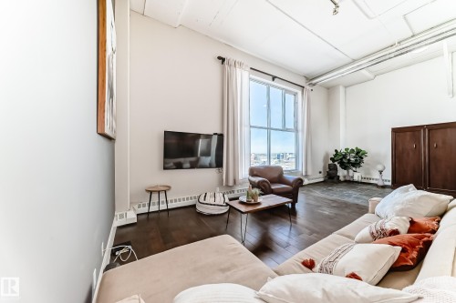 Spacious living area featuring high ceilings, large multi-pane windows, wood-finish flooring, and baseboard heating - 1003 10179 105 Street Nw, Edmonton, AB - Indoor Photo Showing Living Room