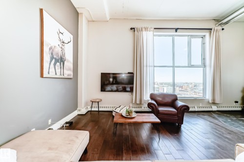 Living area featuring expansive window, dark wood-finish flooring, white baseboards, and light-colored walls with one accent wall - 1003 10179 105 Street Nw, Edmonton, AB - Indoor Photo Showing Living Room