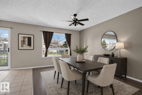 Dining area with wood-finish flooring, a contemporary ceiling fan, and a wide window with dark draperies - 64 3311 58 Street, Edmonton, AB - Indoor Photo Showing Dining Room