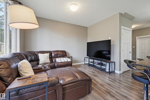 Living area featuring wood-finish flooring, a contemporary ceiling light fixture, a large window, a flat-panel door, and neutral wall paint - 11 94 Longview Drive, Spruce Grove, AB - Indoor Photo Showing Living Room