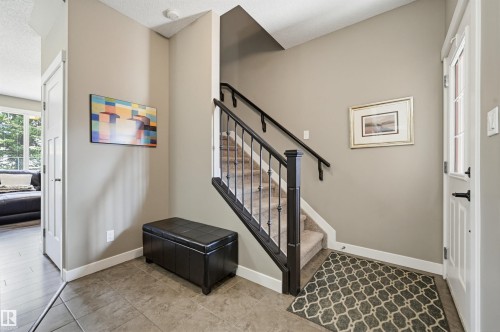 Entryway featuring large format tile flooring, a carpeted staircase with wrought iron balusters and a dark wood handrail, and a white paneled entry door with frosted glass inserts - 11 94 Longview Drive, Spruce Grove, AB - Indoor Photo Showing Other Room