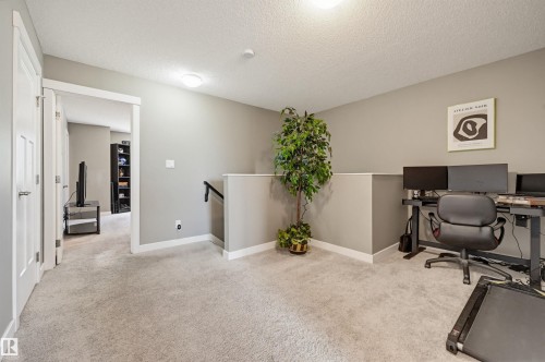 Carpeted interior area with neutral wall paint and white trim, featuring a partial wall with a black handrail, two white paneled doors, and ceiling-mounted flush lighting - 11 94 Longview Drive, Spruce Grove, AB - Indoor
