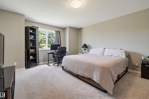 Spacious bedroom featuring light neutral wall tones, plush carpet flooring, a large window offering natural light, and an overhead ceiling fixture - 11 94 Longview Drive, Spruce Grove, AB - Indoor Photo Showing Bedroom