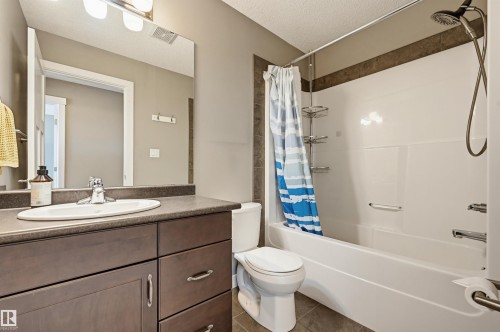 Bathroom featuring a dark wood-finish vanity with an oval sink, a large mirror, a chrome faucet, and a shower-tub combination with a tiled accent wall - 11 94 Longview Drive, Spruce Grove, AB - Indoor Photo Showing Bathroom