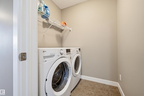 Dedicated laundry area featuring a front-loading washer and dryer, a wire shelving unit, neutral wall paint, and tile flooring - 11 94 Longview Drive, Spruce Grove, AB - Indoor Photo Showing Laundry Room
