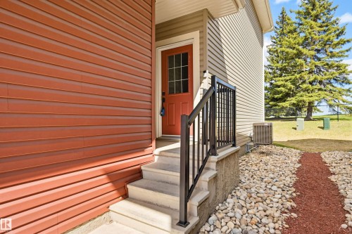 Entryway featuring a red paneled door with glass inserts, concrete steps, and a black metal railing - 11 94 Longview Drive, Spruce Grove, AB - Outdoor With Exterior