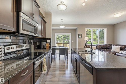 Kitchen featuring dark wood-finish cabinetry, stainless steel appliances, dark subway tile backsplash, and stone countertops - 11 94 Longview Drive, Spruce Grove, AB - Indoor Photo Showing Kitchen With Stainless Steel Kitchen With Double Sink With Upgraded Kitchen