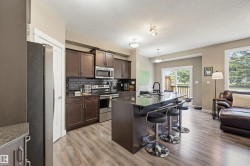 Open-concept kitchen featuring dark wood cabinetry, stainless steel appliances, a black subway tile backsplash, a central island with an integrated sink, and wood-finish flooring - 