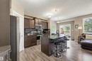 Open-concept kitchen featuring dark wood cabinetry, stainless steel appliances, a black subway tile backsplash, a central island with an integrated sink, and wood-finish flooring - 11 94 Longview Drive, Spruce Grove, AB  - Indoor Photo Showing Kitchen With Stainless Steel Kitchen 