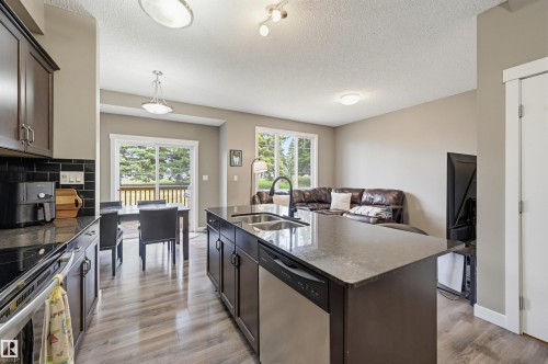 Modern kitchen featuring dark cabinetry, dark countertops, and wood-finish flooring - 11 94 Longview Drive, Spruce Grove, AB - Indoor Photo Showing Kitchen With Stainless Steel Kitchen With Double Sink With Upgraded Kitchen