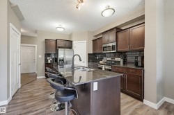 Kitchen featuring a large central island with seating, dark wood-finish cabinetry, stainless steel appliances, dark subway tile backsplash, and wood-finish flooring - 