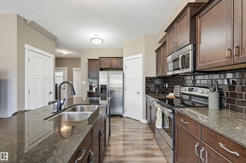 Kitchen featuring dark wood cabinetry, a large island with an undermount double sink, and dark stone countertops - 11 94 Longview Drive, Spruce Grove, AB - Indoor Photo Showing Kitchen With Stainless Steel Kitchen With Double Sink With Upgraded Kitchen
