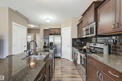 Kitchen featuring dark wood cabinetry, a large island with an undermount double sink, and dark stone countertops - 