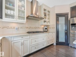 Kitchen featuring light-toned cabinetry, granite-finish countertops, stainless steel appliances, a five-burner gas cooktop, and wood-finish flooring - 