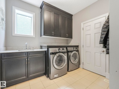 Utility room with light-toned tiled flooring, dark wood-finish cabinetry, light-toned countertop, and an integrated sink with a chrome faucet - 932 Summerside Link, Edmonton, AB - Indoor Photo Showing Laundry Room