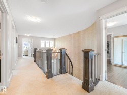 Upper-level hallway featuring plush carpeting, a curved accent wall, and a staircase with dark wood newel posts and railings - 
