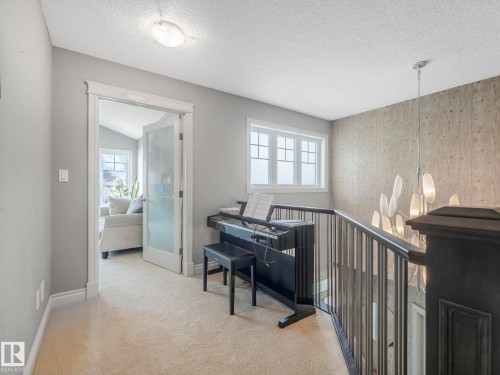 Upper-level landing featuring plush carpeting, a modern chandelier, and a wood-panel accent wall - 932 Summerside Link, Edmonton, AB - Indoor Photo Showing Other Room