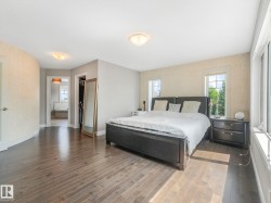 Spacious bedroom featuring wood-finish flooring, multiple windows, and a doorway opening to an additional room with a built-in tub - 