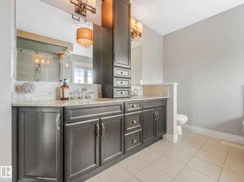 Dual vanity with granite countertop, integrated sinks, dark wood cabinetry, and a tall storage tower - 932 Summerside Link, Edmonton, AB - Indoor Photo Showing Bathroom