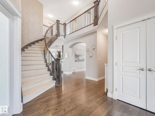 Grand entryway featuring a curved staircase with dark wood-finish banister and carpeted treads, wood-finish flooring, and a second-story landing with matching banister - 932 Summerside Link, Edmonton, AB - Indoor Photo Showing Other Room