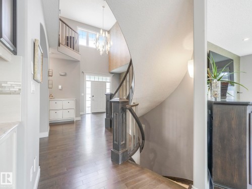 Grand foyer featuring a dark wood-finish flooring, a two-story ceiling, and a prominent curved staircase with dark wood newel posts and railings - 932 Summerside Link, Edmonton, AB - Indoor Photo Showing Other Room