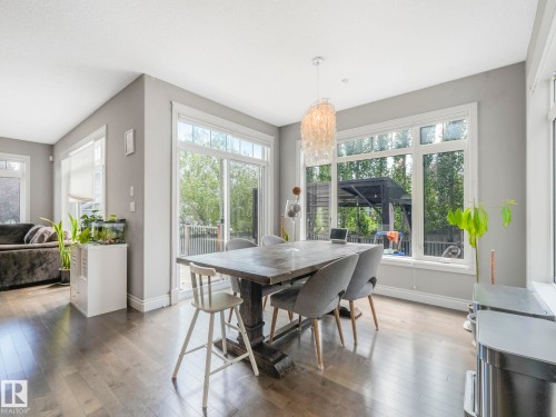 Spacious dining area featuring wood-finish flooring, a contemporary chandelier, multiple large windows, and a sliding glass door - 932 Summerside Link, Edmonton, AB - Indoor Photo Showing Dining Room