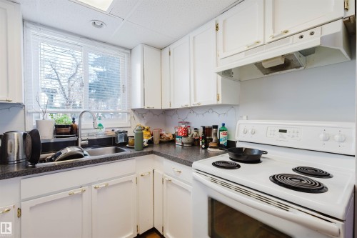 Kitchen featuring white cabinetry, a double-basin stainless steel sink with a gooseneck faucet, a white electric range with a matching range hood, and speckled dark countertops - 10831 80 Avenue, Edmonton, AB - Indoor Photo Showing Kitchen With Double Sink