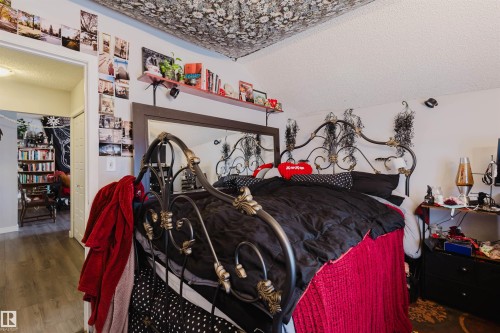Bedroom featuring a decorative metal headboard, a large wall-mounted mirror, and wood-finish flooring - 10831 80 Avenue, Edmonton, AB - Indoor
