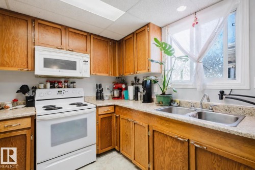 Functional kitchen with wood cabinetry, light-toned countertops, and a white electric range with an overhead microwave - 10831 80 Avenue, Edmonton, AB - Indoor Photo Showing Kitchen With Double Sink