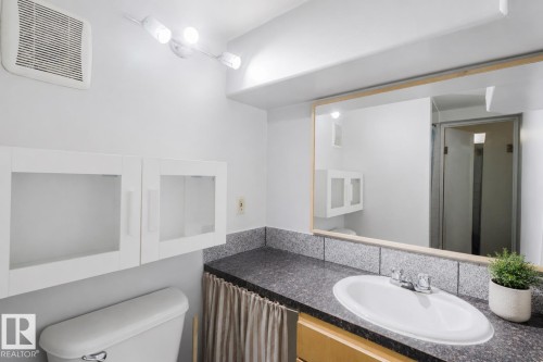 Bathroom vanity with an undermount sink, a dark countertop, and a wood-framed mirror - 10831 80 Avenue, Edmonton, AB - Indoor Photo Showing Bathroom