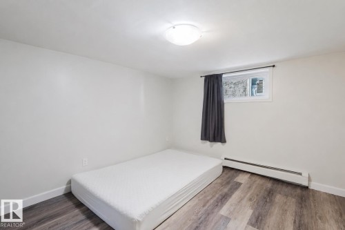 Room featuring wood-finish flooring, a baseboard heating unit, a window with a dark curtain, and a ceiling-mounted light fixture - 10831 80 Avenue, Edmonton, AB - Indoor Photo Showing Bedroom