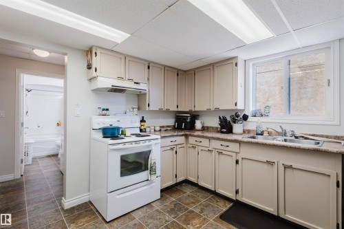 Kitchen featuring cream-colored cabinetry, laminate countertops, a white electric range with overhead vent, and a stainless steel double-basin sink - 10831 80 Avenue, Edmonton, AB - Indoor Photo Showing Kitchen With Double Sink