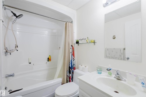 Full bathroom featuring a white tub and shower combination with a handheld shower head, a white vanity with an integrated sink, a wall-mounted mirror, and overhead vanity lighting - 10831 80 Avenue, Edmonton, AB - Indoor Photo Showing Bathroom