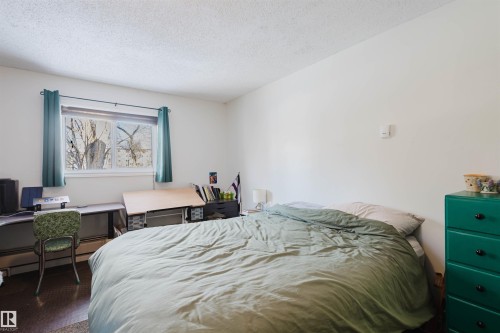 Room featuring a window with teal curtains, white textured ceilings, and wood-finish flooring - 10831 80 Avenue, Edmonton, AB - Indoor Photo Showing Bedroom