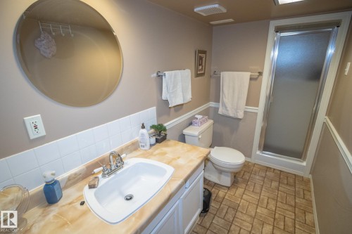 Bathroom featuring a single vanity with an integrated sink, patterned countertop, and a circular wall mirror - 4417 46A St, St. Paul Town, AB - Indoor Photo Showing Bathroom