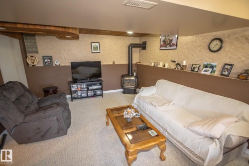 Finished lower level featuring neutral carpeting, a built-in shelf, and a freestanding wood-burning stove with a black stovepipe - 4417 46A St, St. Paul Town, AB - Indoor Photo Showing Living Room