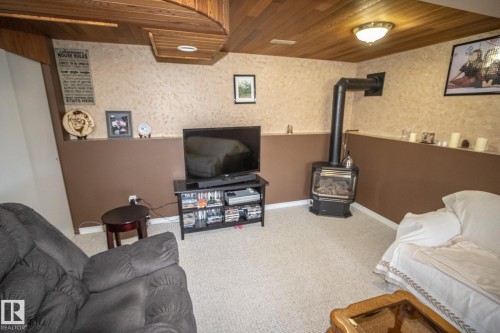 Room featuring a gas stove, wood-panel ceiling, wall-mounted light fixture, carpeted flooring, and a decorative shelf - 4417 46A St, St. Paul Town, AB - Indoor