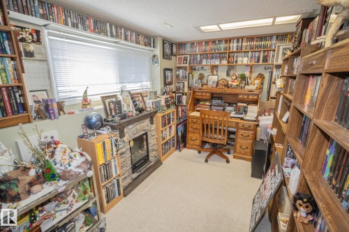 Dedicated room featuring extensive built-in shelving, a stone-finish fireplace, and a large window with horizontal blinds - 4417 46A St, St. Paul Town, AB - Indoor