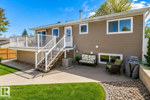 Rear exterior featuring a spacious elevated deck with white railings, a concrete patio, a manicured lawn, and brown horizontal siding - 4417 46A St, St. Paul Town, AB - Outdoor With Deck Patio Veranda With Exterior