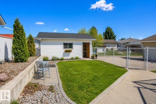 Detached white siding structure featuring a dark shingle roof, a window with a built-in planter box, and an open doorway revealing interior shelving - 4417 46A St, St. Paul Town, AB - Outdoor