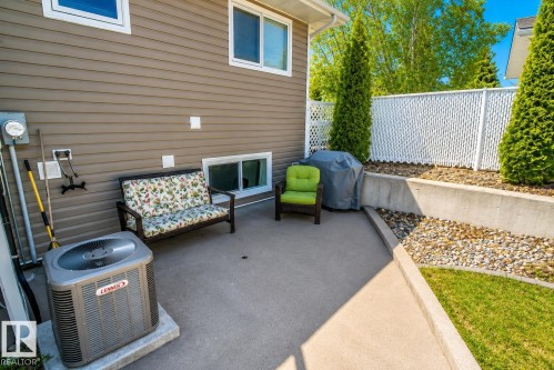 Concrete patio with a retaining wall, accented by a decorative lattice fence and manicured evergreen trees - 4417 46A St, St. Paul Town, AB - Outdoor With Exterior