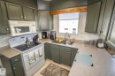 Kitchen featuring painted shaker-style cabinetry, a stainless steel sink with a gooseneck faucet, a white electric range with an overhead microwave, and light-toned countertops - 4417 46A St, St. Paul Town, AB  - Indoor Photo Showing Kitchen 