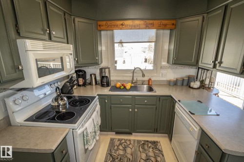 U-shaped kitchen featuring painted green cabinetry, light-colored countertops, a white tile backsplash, an undermount sink with a gooseneck faucet, and white appliances including a range with an over-the-range microwave and a dishwasher - 4417 46A St, St. Paul Town, AB - Indoor Photo Showing Kitchen