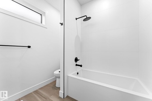 The bathroom features a white bathtub with matte black fixtures, white tile shower surround, and a toilet - 11019 132 St, Edmonton, AB - Indoor Photo Showing Bathroom