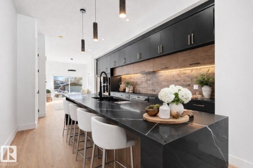 The kitchen features a spacious island with a dark countertop and seating, complemented by dark cabinetry and a light wood backsplash - 11019 132 St, Edmonton, AB - Indoor