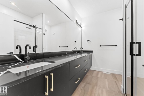 Modern bathroom featuring a double vanity with a dark countertop and gold hardware, a large mirror, and a glass-enclosed shower with black framing - 11019 132 St, Edmonton, AB - Indoor Photo Showing Bathroom