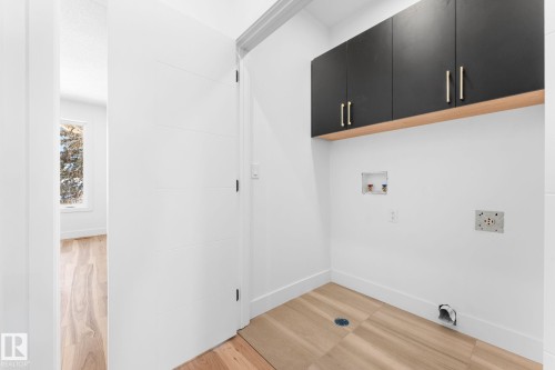 Utility area with light wood-style flooring, black upper cabinets with gold-toned hardware, and a window providing natural light - 11019 132 St, Edmonton, AB - Indoor Photo Showing Other Room