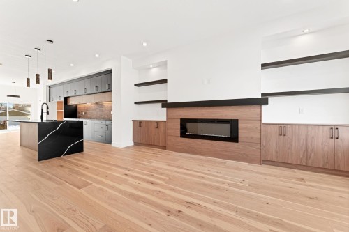 The living area features light wood flooring, a fireplace with a wood surround, and built-in shelving - 11019 132 St, Edmonton, AB - Indoor Photo Showing Living Room With Fireplace