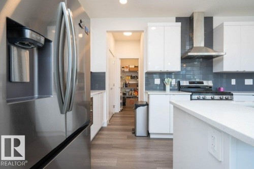 Kitchen featuring stainless steel appliances, white cabinetry, a tile backsplash, light wood-finish flooring, and a walk-in pantry - 5627 Kootook Place, Edmonton, AB - Indoor Photo Showing Kitchen