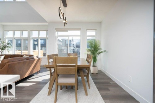 Bright dining area featuring wood-finish flooring, a modern linear chandelier with circular accents, and large windows providing abundant natural light - 5627 Kootook Place, Edmonton, AB - Indoor Photo Showing Dining Room
